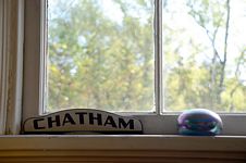 Wooden “Chatham” sign on windowframe beside a dark ceramic container with multi-color sheen.